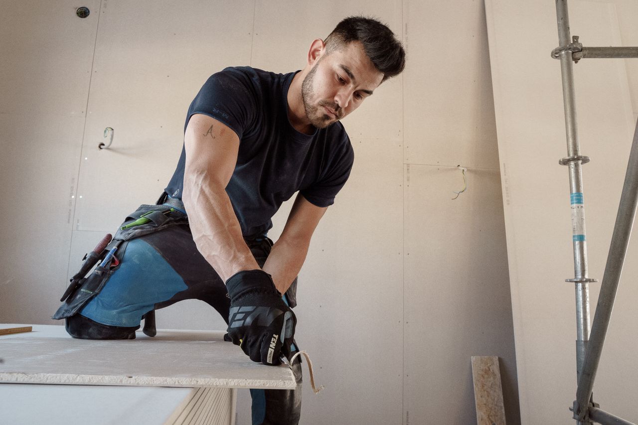 The Art of Drawing Readers In: Your attractive post title goes here Man in gloves cutting plasterboard for drywall installation inside a building.
