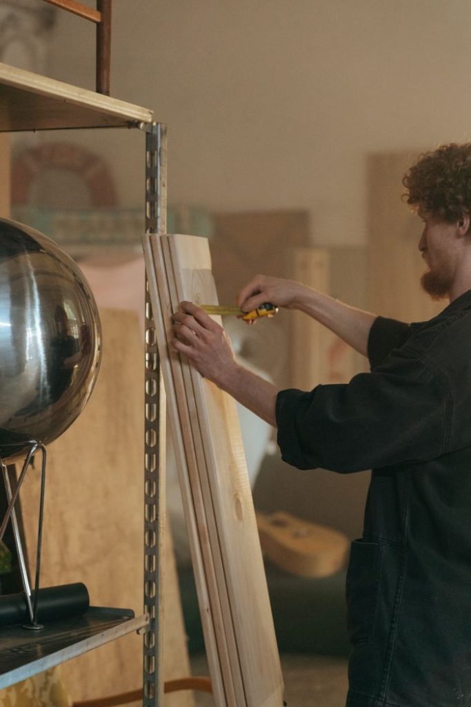 A male craftsman measuring wooden planks in a workshop, highlighting carpentry skills.